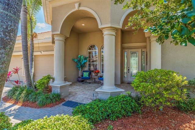 view of exterior entry with stucco siding, a garage, and french doors
