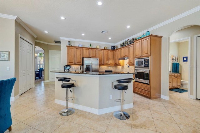 kitchen featuring arched walkways, backsplash, light tile patterned floors, and appliances with stainless steel finishes