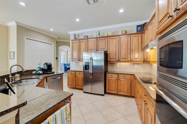 kitchen featuring under cabinet range hood, a sink, stone counters, arched walkways, and appliances with stainless steel finishes