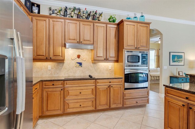 kitchen featuring ornamental molding, stainless steel appliances, dark stone countertops, under cabinet range hood, and arched walkways