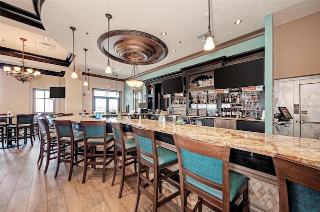 kitchen featuring light wood finished floors, light stone countertops, hanging light fixtures, and ornamental molding