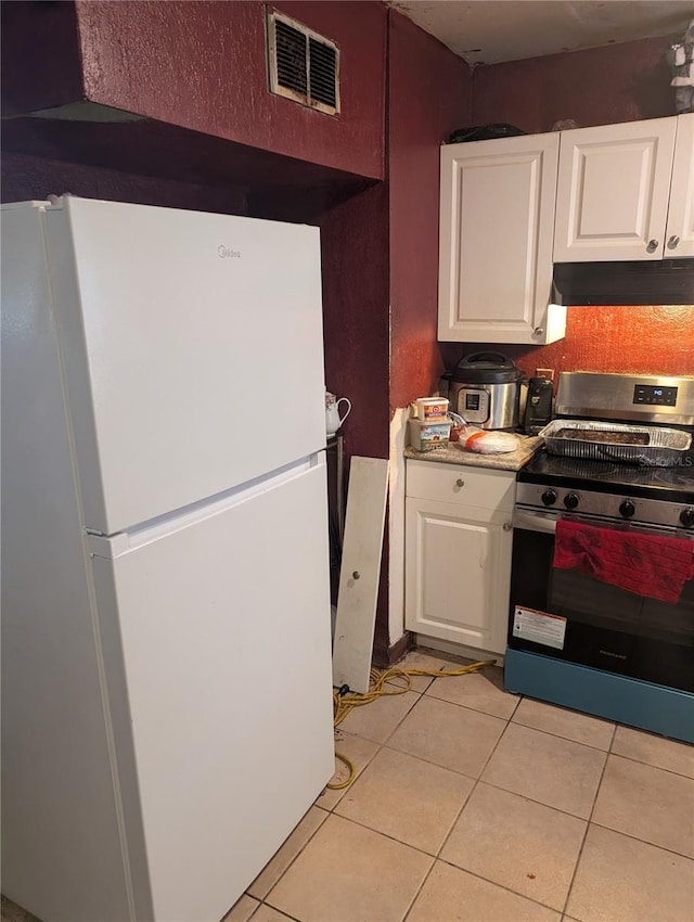 5195 Edwina St, Orlando, FL 32811 - kitchen featuring visible vents, under cabinet range hood, light tile patterned floors, freestanding refrigerator, and electric stove