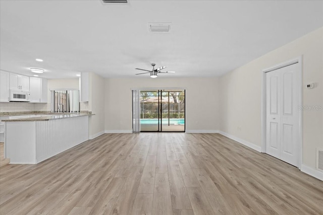 unfurnished living room with light wood-style floors, a ceiling fan, visible vents, and baseboards