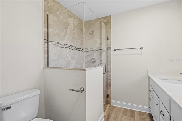 bathroom with toilet, a stall shower, wood finished floors, baseboards, and vanity