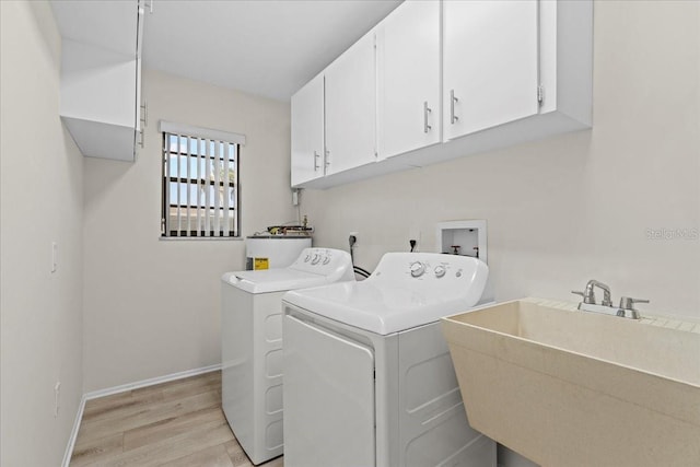 laundry area with baseboards, cabinet space, a sink, light wood-type flooring, and washer and clothes dryer