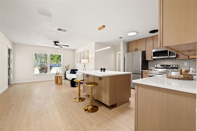 6639 16th St N, Saint Petersburg, FL 33702 - kitchen with a kitchen island, ceiling fan, decorative backsplash, stainless steel appliances, and light wood-type flooring