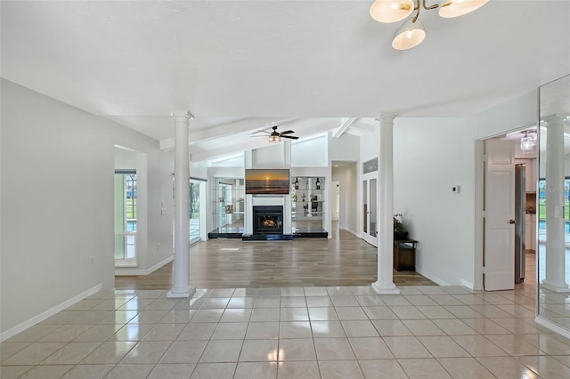 unfurnished living room featuring a lit fireplace, lofted ceiling, light tile patterned floors, decorative columns, and a ceiling fan