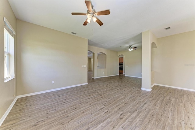 spare room with arched walkways, visible vents, light wood-style floors, and ceiling fan