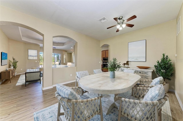 dining area featuring light wood-type flooring, visible vents, arched walkways, baseboards, and ceiling fan