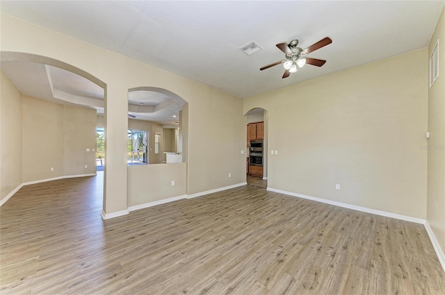 unfurnished living room featuring light wood-style flooring, a ceiling fan, visible vents, and baseboards