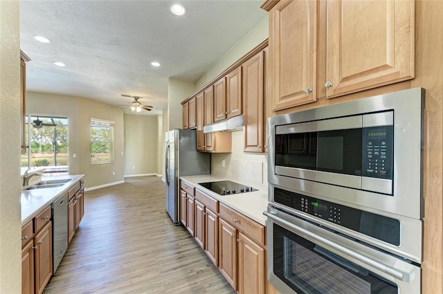 kitchen with ceiling fan, stainless steel appliances, light countertops, light wood-style floors, and under cabinet range hood