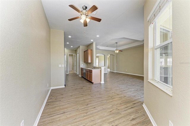 unfurnished living room featuring arched walkways, light wood-style flooring, a ceiling fan, and a sink