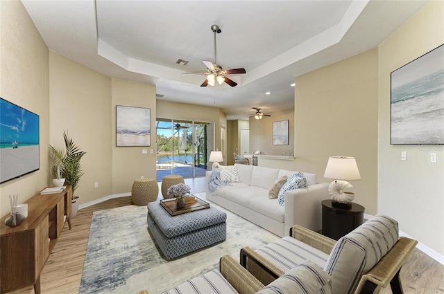 living area with a tray ceiling, baseboards, light wood finished floors, and ceiling fan