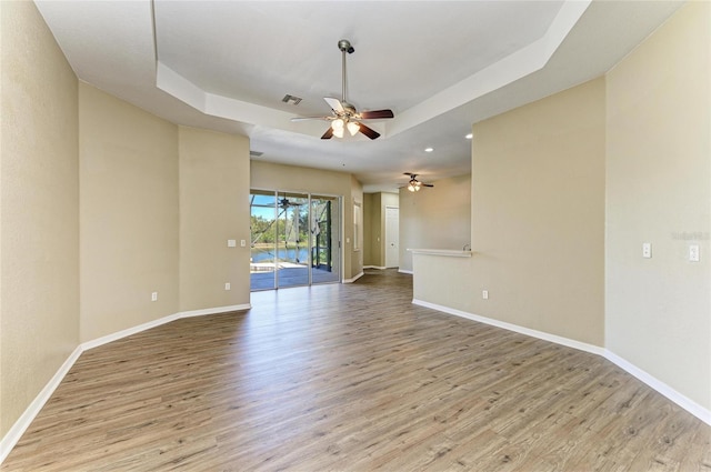 unfurnished room with ceiling fan, a tray ceiling, baseboards, and wood finished floors