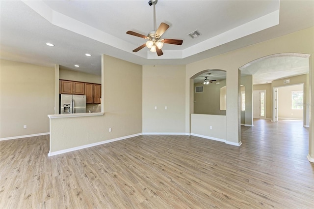 unfurnished living room featuring light wood finished floors, visible vents, a tray ceiling, and a ceiling fan