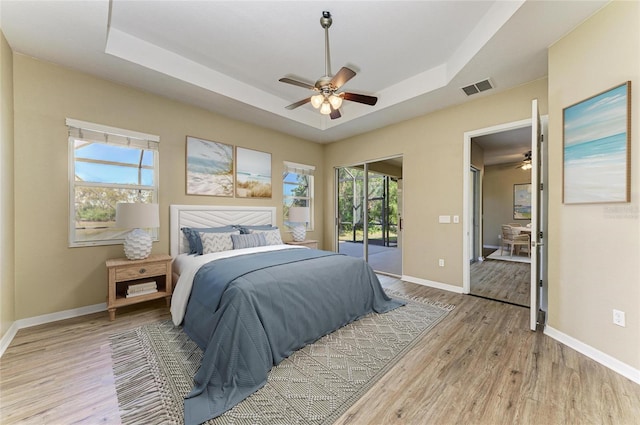 bedroom featuring a tray ceiling, light wood-style floors, visible vents, and access to exterior