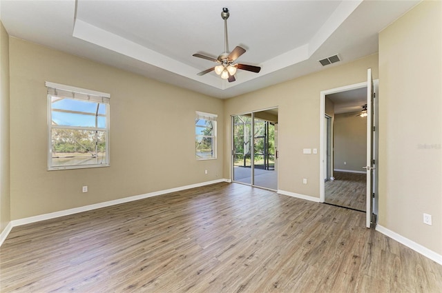unfurnished bedroom with visible vents, light wood-style flooring, access to outside, baseboards, and a raised ceiling