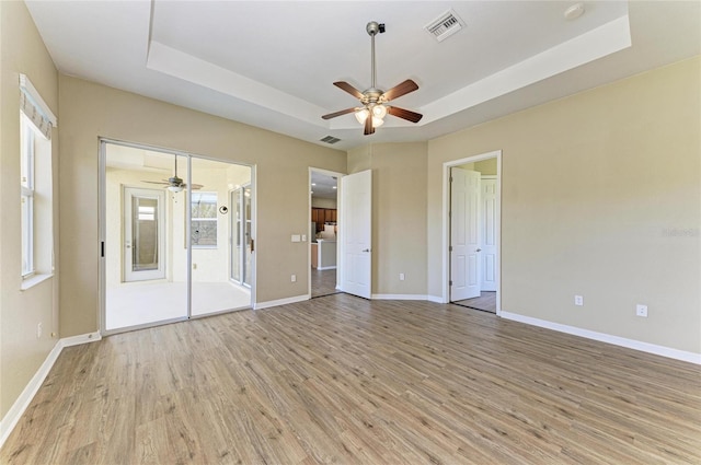 unfurnished bedroom featuring a tray ceiling, light wood-style flooring, baseboards, and visible vents