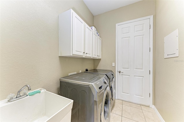 laundry area featuring a sink, baseboards, light tile patterned floors, cabinet space, and separate washer and dryer