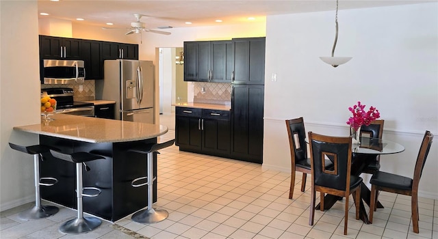 kitchen featuring ceiling fan, backsplash, stainless steel appliances, and dark cabinetry