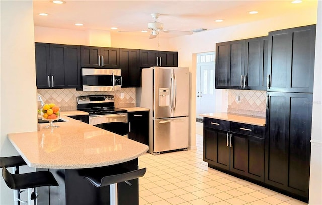 kitchen with decorative backsplash, a kitchen bar, a peninsula, appliances with stainless steel finishes, and visible vents