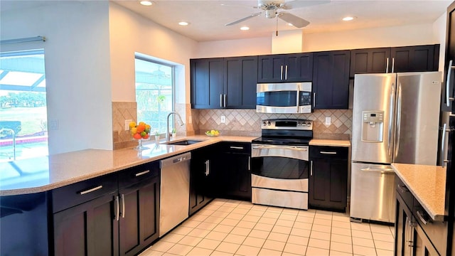 kitchen featuring stainless steel appliances, a sink, light tile patterned flooring, decorative backsplash, and a ceiling fan