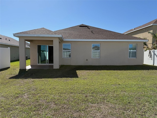 rear view of property with stucco siding, roof with shingles, a yard, and fence