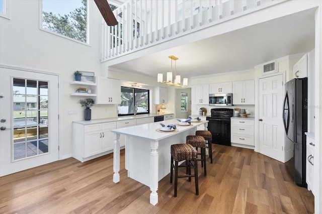 4406 17th St W, Palmetto, FL 34221 - kitchen featuring black appliances, healthy amount of natural light, a breakfast bar area, white cabinets, and a towering ceiling