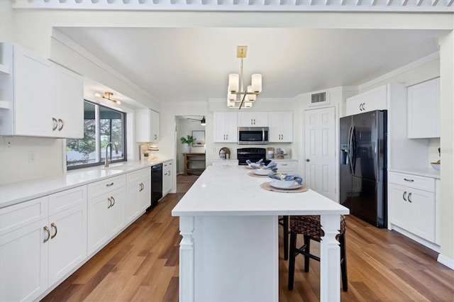 4406 17th St W, Palmetto, FL 34221 - kitchen featuring black appliances, a chandelier, a kitchen island, a breakfast bar, and white cabinets