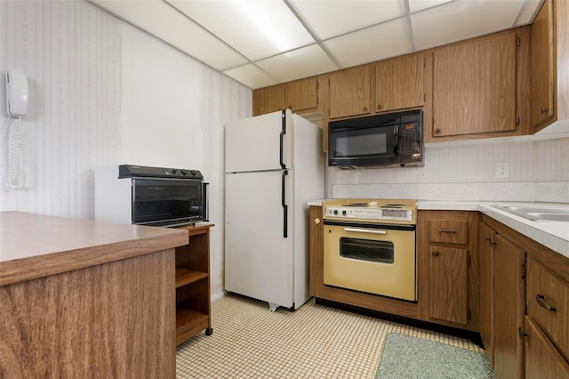 kitchen featuring electric range oven, black microwave, freestanding refrigerator, light countertops, and a paneled ceiling