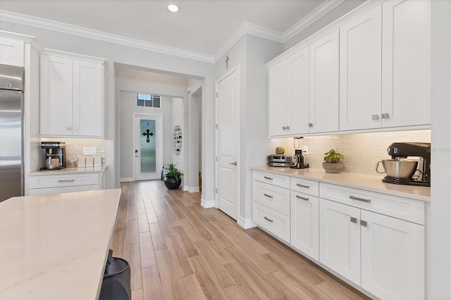 kitchen featuring baseboards, ornamental molding, white cabinetry, light wood-type flooring, and backsplash