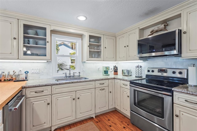 111 Faubel St, Sarasota, FL 34242 - kitchen featuring light wood-type flooring, backsplash, a sink, appliances with stainless steel finishes, and glass insert cabinets