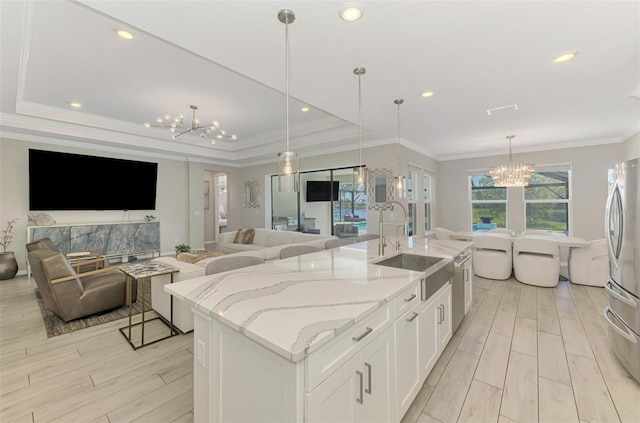 kitchen with a sink, freestanding refrigerator, light wood-style floors, a notable chandelier, and an island with sink