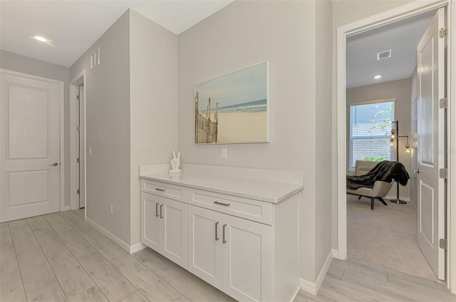 corridor with baseboards, visible vents, and light wood-style floors