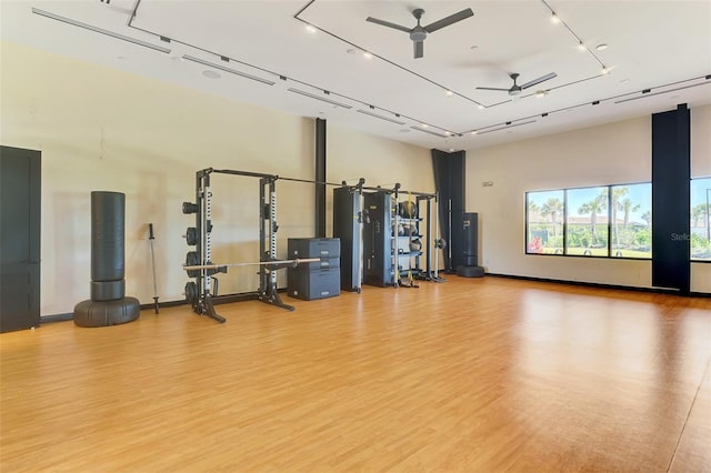 gym with a towering ceiling, a ceiling fan, and light wood-style floors