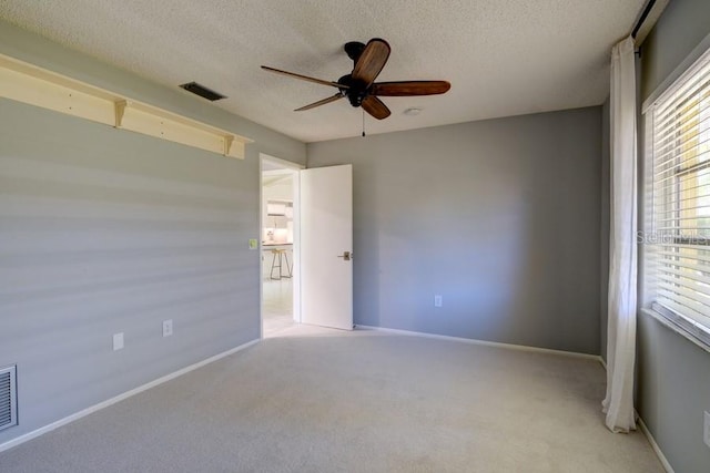 spare room with a ceiling fan, a textured ceiling, baseboards, light colored carpet, and visible vents
