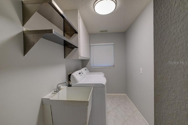 washroom featuring light tile patterned flooring, a textured ceiling, laundry area, a sink, and washer and clothes dryer