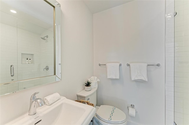 bathroom featuring toilet, tiled shower, and a sink