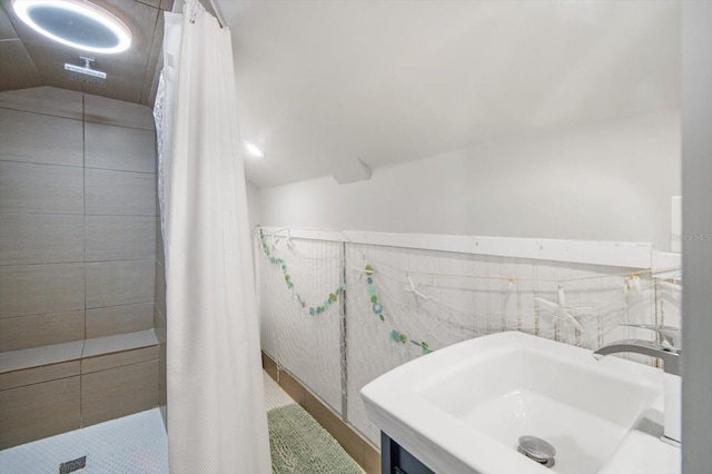 bathroom with a tile shower, vaulted ceiling, and a sink
