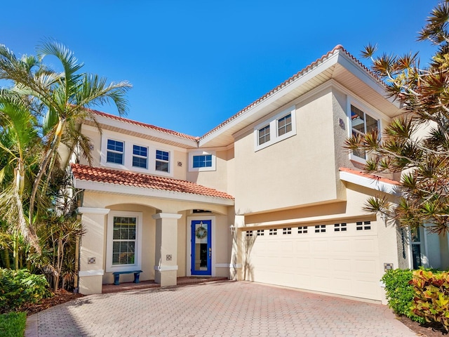 mediterranean / spanish-style home featuring a tile roof, a garage, decorative driveway, and stucco siding
