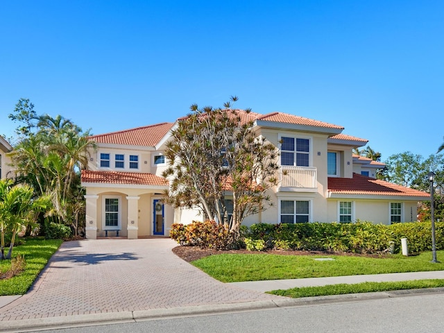 mediterranean / spanish house featuring a front lawn, decorative driveway, a tile roof, and stucco siding