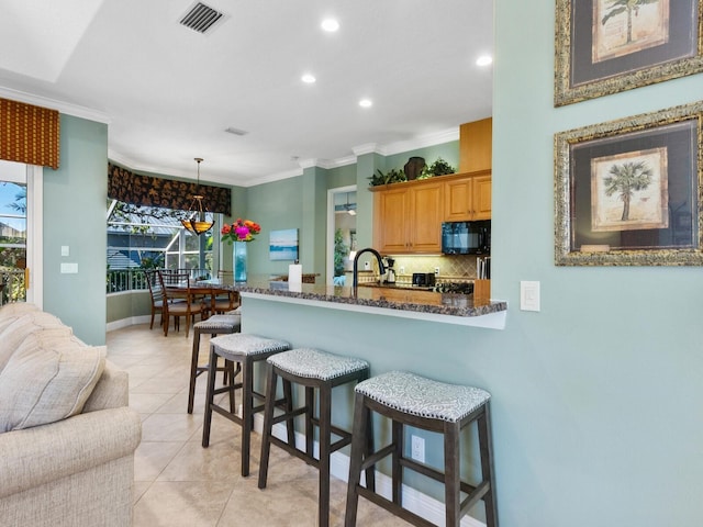 kitchen featuring ornamental molding, tasteful backsplash, black microwave, a kitchen breakfast bar, and light tile patterned floors