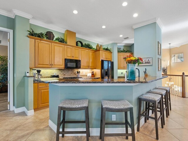 kitchen featuring crown molding, a breakfast bar area, black appliances, and backsplash