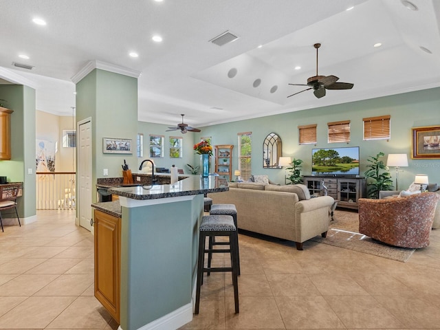 kitchen featuring a kitchen breakfast bar, open floor plan, visible vents, ceiling fan, and ornamental molding