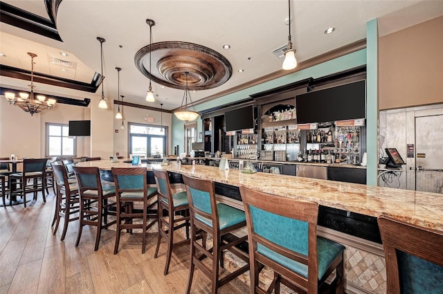 kitchen featuring light wood finished floors, light stone countertops, ornamental molding, pendant lighting, and a notable chandelier