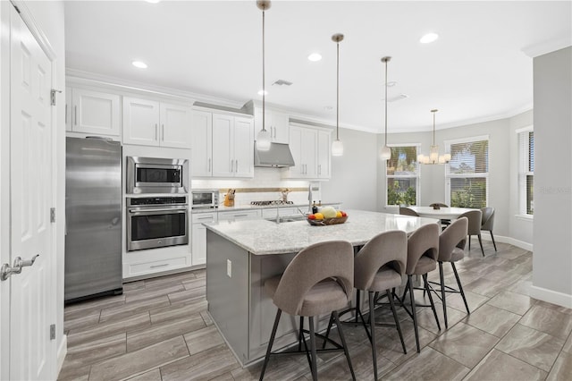5954 Anise Dr, Sarasota, FL 34238 - kitchen with appliances with stainless steel finishes, under cabinet range hood, a kitchen island with sink, white cabinets, and a chandelier