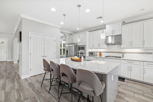 5954 Anise Dr, Sarasota, FL 34238 - kitchen with stainless steel appliances, under cabinet range hood, ornamental molding, a center island with sink, and decorative backsplash