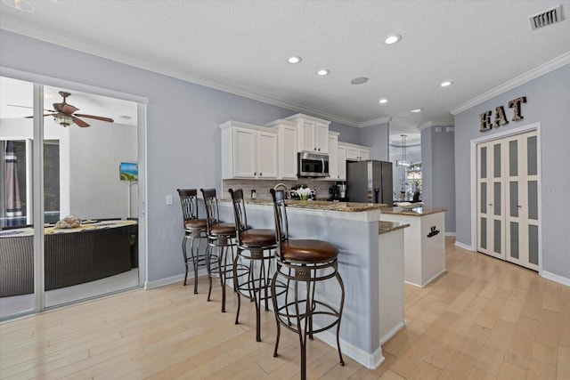 259 Golden Harbour Trl, Bradenton, FL 34212 - kitchen with visible vents, appliances with stainless steel finishes, a peninsula, light wood-style floors, and white cabinetry