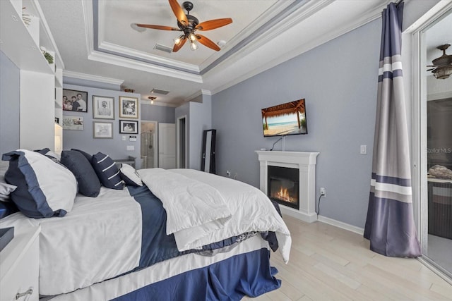 259 Golden Harbour Trl, Bradenton, FL 34212 - bedroom featuring light wood finished floors, visible vents, a tray ceiling, ornamental molding, and a glass covered fireplace