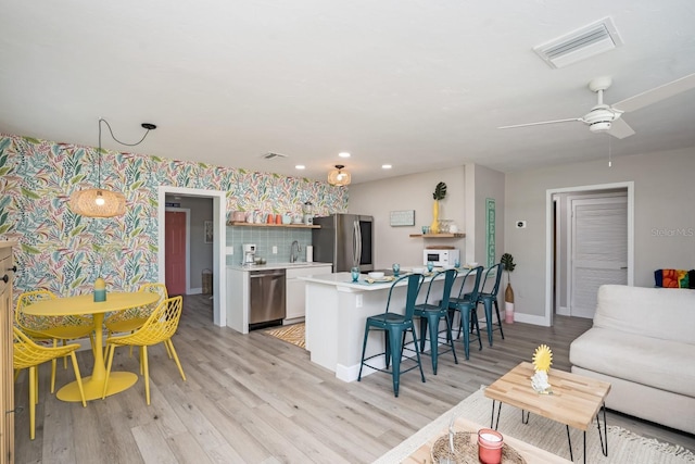 kitchen featuring light countertops, visible vents, stainless steel appliances, a sink, and a kitchen breakfast bar